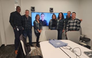 Seven Northwestern Mutual teammates stand in a conference room in front of a screen with a virtual teammate.